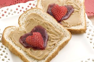 Dos rebanadas de pan de trigo entero con mantequilla de maní, mermelada y fresa.