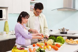 Mujer asiática embarazada preparando la cena con su esposo.