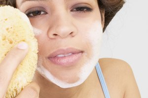 Una mujer joven enjabona su rostro con un limpiador.