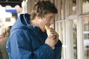 Hombre comiendo bocadillo mientras mira la vitrina de una tienda.