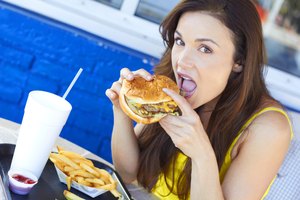 Mujer joven comiendo una hamburguesa con papas fritas.