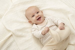 Baby girl (3-6 months) lying on blanket, smiling