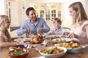 Familia feliz comiendo pollo asado en la mesa.
