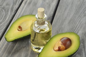 Una botella de aceite de aguacate en una mesa con un aguacate a la mitad.