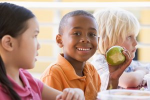 Un niño come una manzana verde en la cafetería de la escuela.