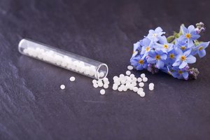 Tabletas homeopáticas en un frasco de píldoras junto a flores de borraja.