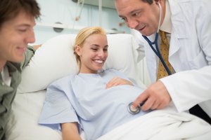 Obstetra sonriendo usa estetoscopio en mujer embarazada.