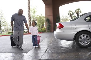 Father and daughter (4-5 years) walking with suitcases through hotel driveway