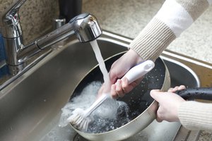 Una persona enjuaga una olla y la limpia con un cepillo