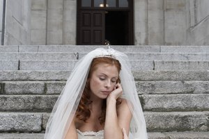 Bride sitting on stone steps, hand to face, looking towards ground