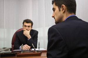 An employee looks to his side as his boss sits in the background listening to an unseen person during a meeting.