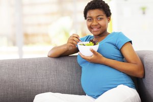 Mujer embarazada comiendo ensalada en un sofá.