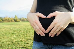 Una mujer embarazada hace una forma de corazón con sus manos al aire libre.