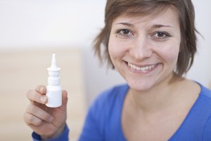 Mujer sosteniendo botella de aerosol nasal salino.