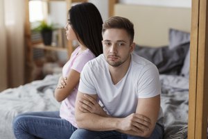 Offended Couple Sitting On Different Sides Of Bed At Home