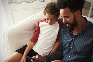Father And Son Sitting On Sofa Using Digital Tablet