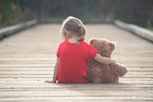 Little girl in red dress sitting on boardwalk hugging teddybear