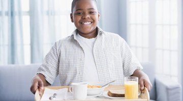 Young boy holding up a breakfast tray.