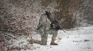 Army officer kneeling in the snow with gun.