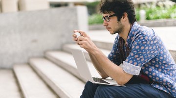 Student sitting on university steps with laptop and smart phone