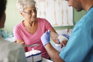 A medical assistant bandages an elderly patient's hand A medical assistant bandages an elderly patient's hand