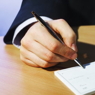 Close-up of man's hand signing cheque