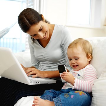 mother working on laptop while baby daughter (12-18 months) playing with mobile phone