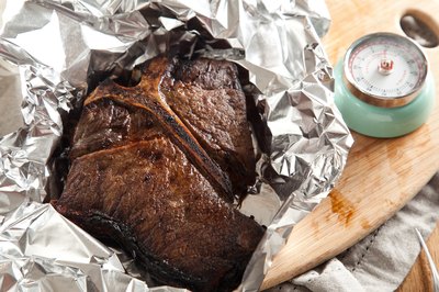 Kitchen timer next to steak cover loosely with aluminum foil.