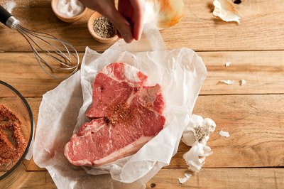 Raw t-bone steak sprinkled with dry spices.