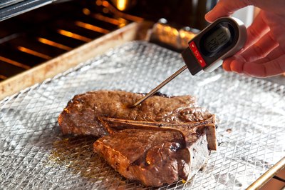 Thermometer in steak on broiler pan in oven.