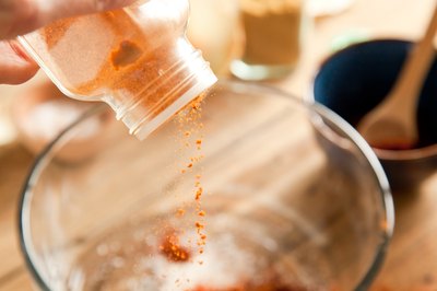 Cumin added to a glass mixing bowl of ingredients.