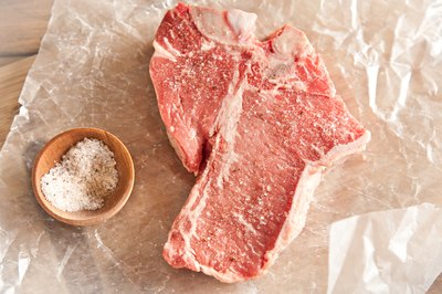 Raw t-bone steak on butcher paper with salt.