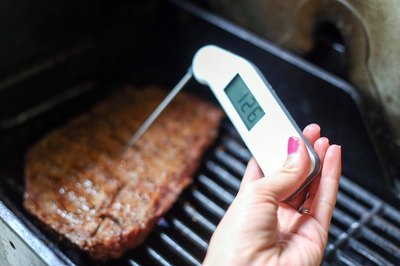 Thermometer reading the temperature of skirt steak on a grill.