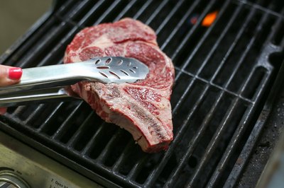 Putting rib steak on grill.