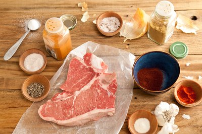 Raw t-bone steak with spices and olive oil on a cutting board.