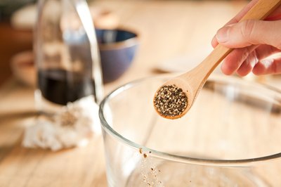 Black pepper in a measuring spoon over a glass mixing bowl.