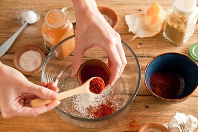 Paprika in a measuring spoon added to a glass mixing bowl of ingredients.