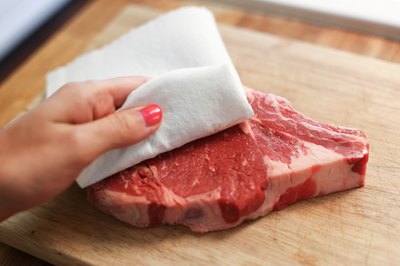 Blotting a rib steak with a paper towel.