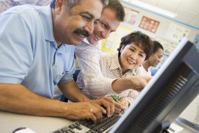 A mature student works at a computer with an instructor.
