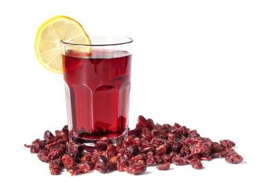 Cranberries surrounding a glass of cranberry juice with a lemon slice