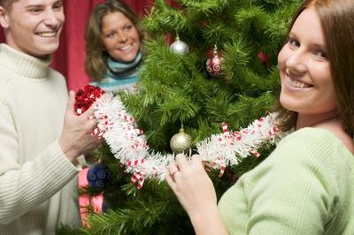3 people smiling and decorating a Christmas tree.