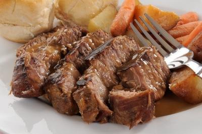 Beef roast served with gravy, vegetables, and rolls.
