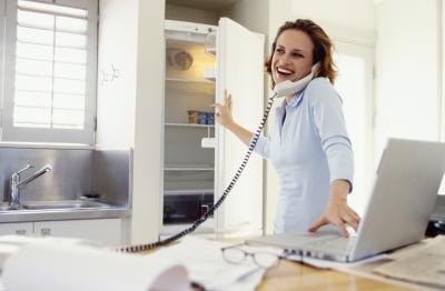 Woman on phone and laptop in kitchen