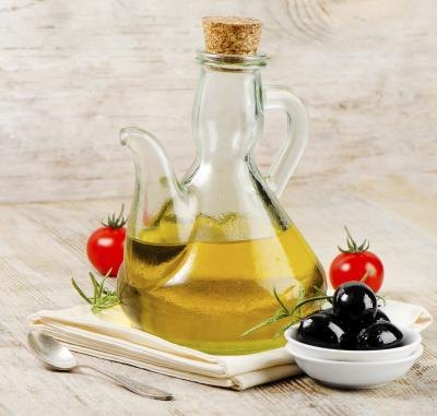 A bottle of olive oil with a some black olives and tomatoes
