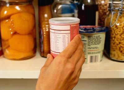 Hand reaching for canned food with nutrition label visible.