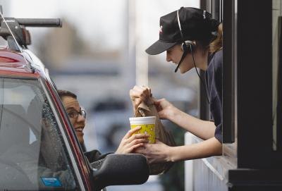 A fast-food employee hands a customer her order from a drive-thru window.