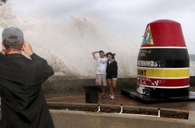 Couple pose by southernmost buoy marker as wave crashes behind in Key West, FL.