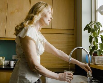 Woman pouring glass of water from sink and looking out window.