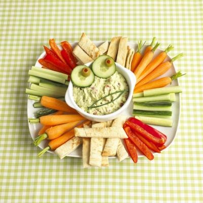 Bowl of guacamole surrounded by pieces of pita bread and raw vegetables