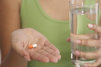 Woman holding capsule and glass of water.